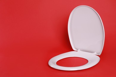 New pink plastic toilet seat on red background, space for text