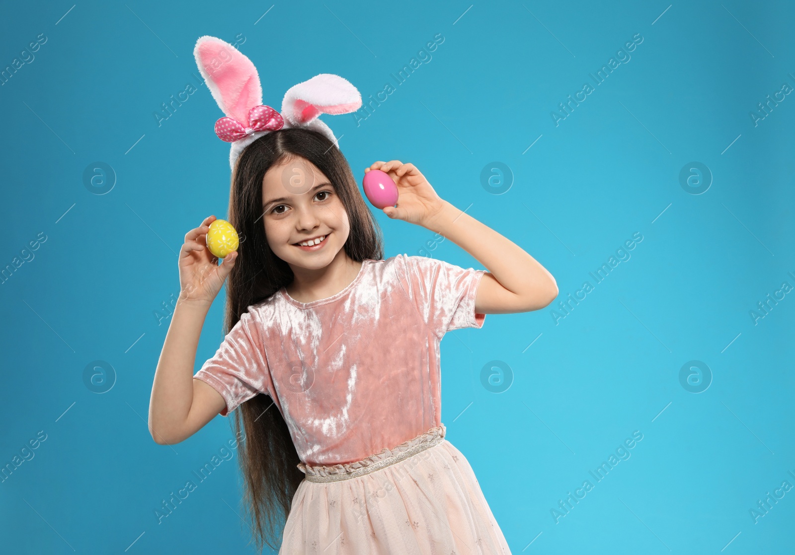 Photo of Little girl in bunny ears headband holding Easter eggs on color background, space for text