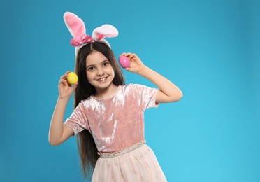 Photo of Little girl in bunny ears headband holding Easter eggs on color background, space for text