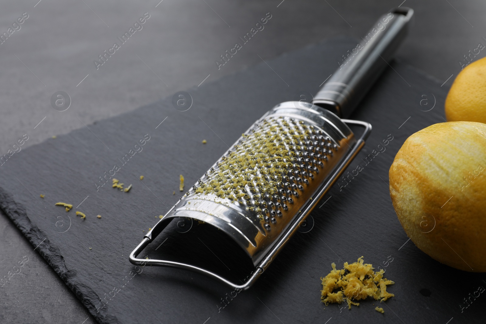 Photo of Grater and fresh lemons on black table