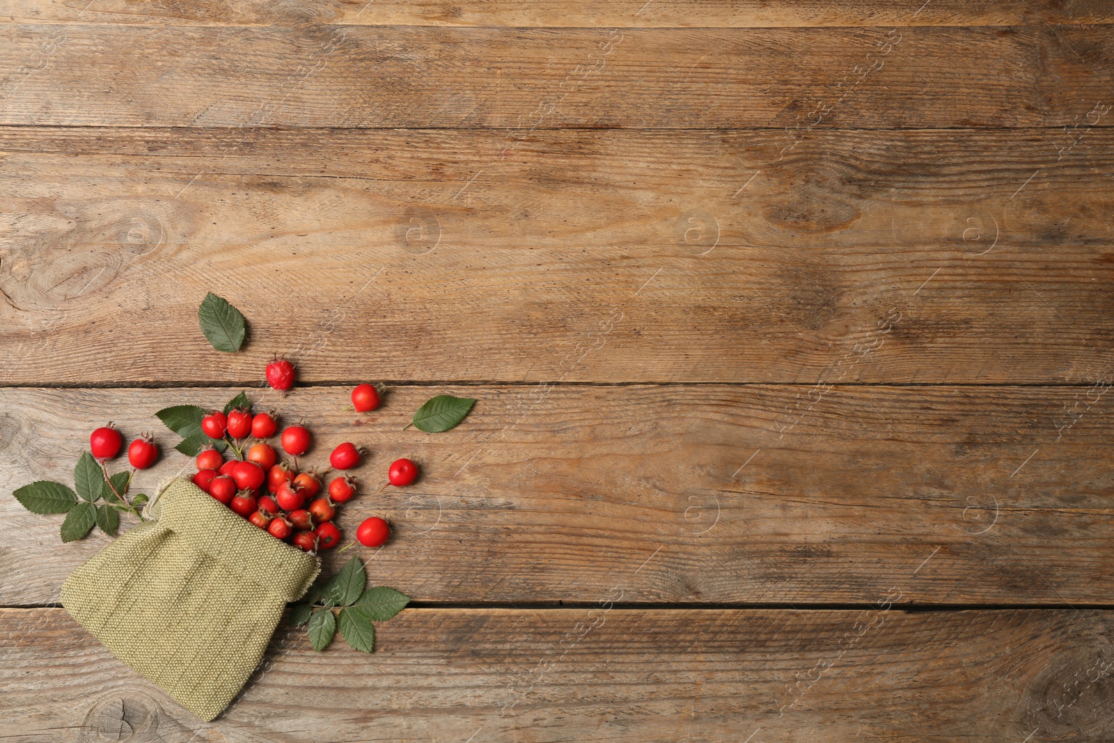 Photo of Ripe rose hip berries with green leaves on wooden table, flat lay. Space for text