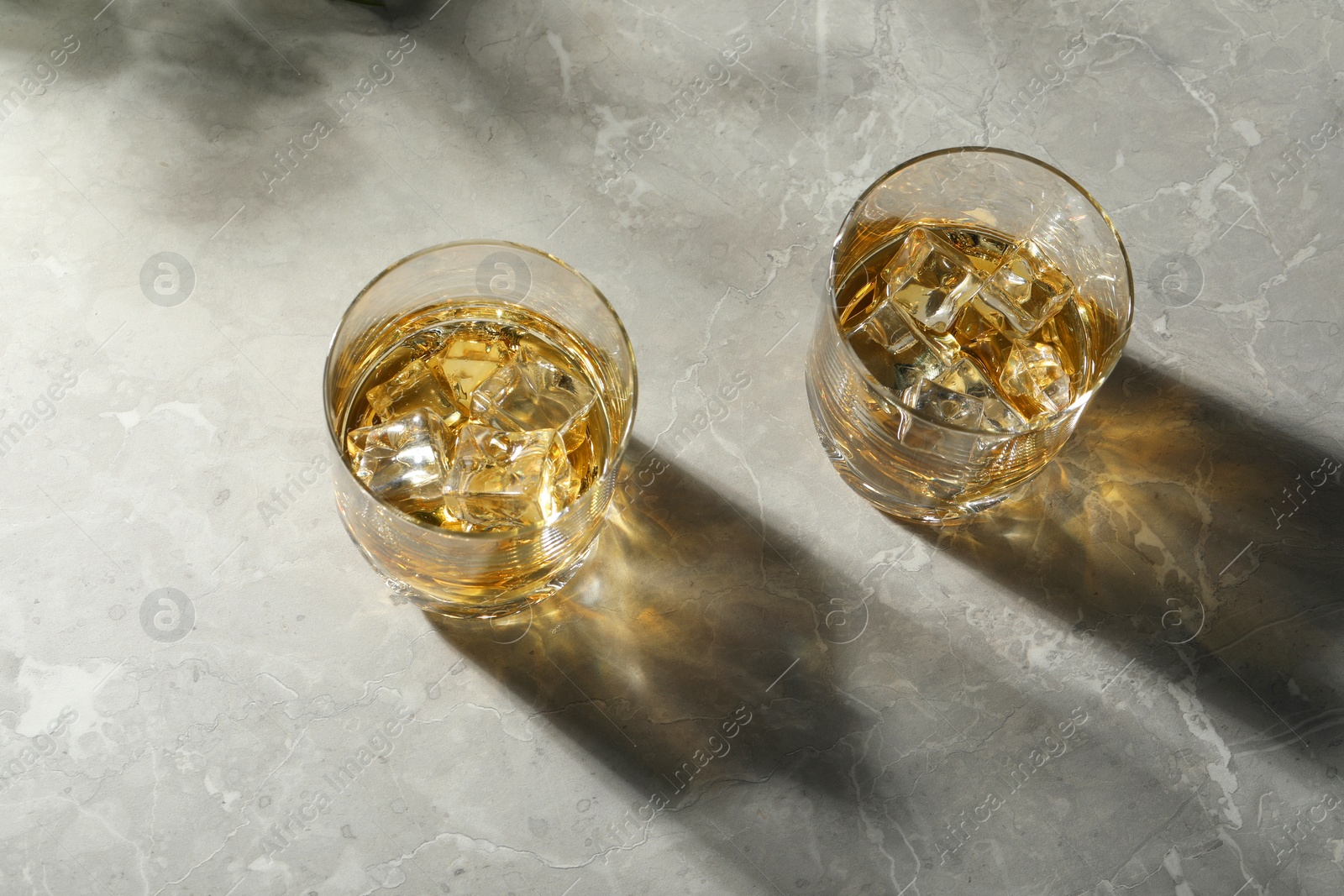 Photo of Whiskey with ice cubes in glasses on grey marble table, above view