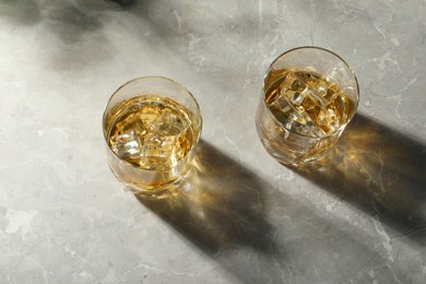 Whiskey with ice cubes in glasses on grey marble table, above view