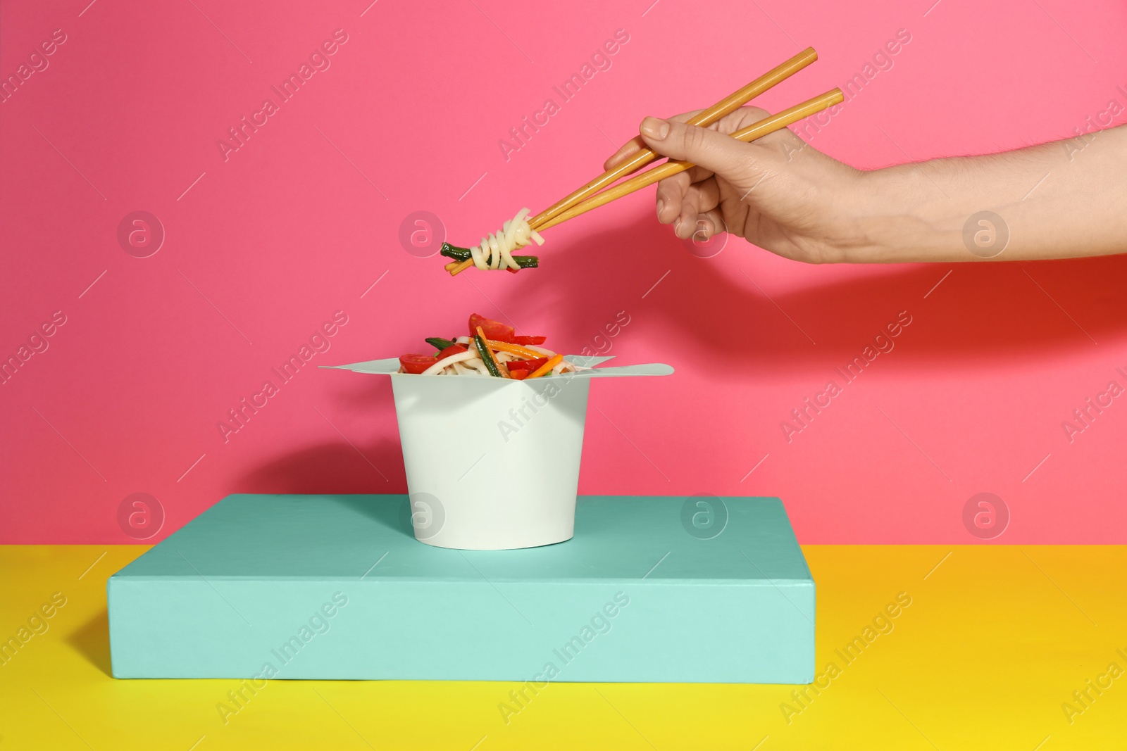 Photo of Woman eating vegetarian wok noodles with chopsticks from box on color background, closeup