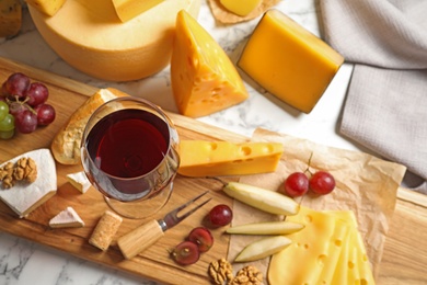 Board with different kinds of delicious cheese, snacks and wine on marble table