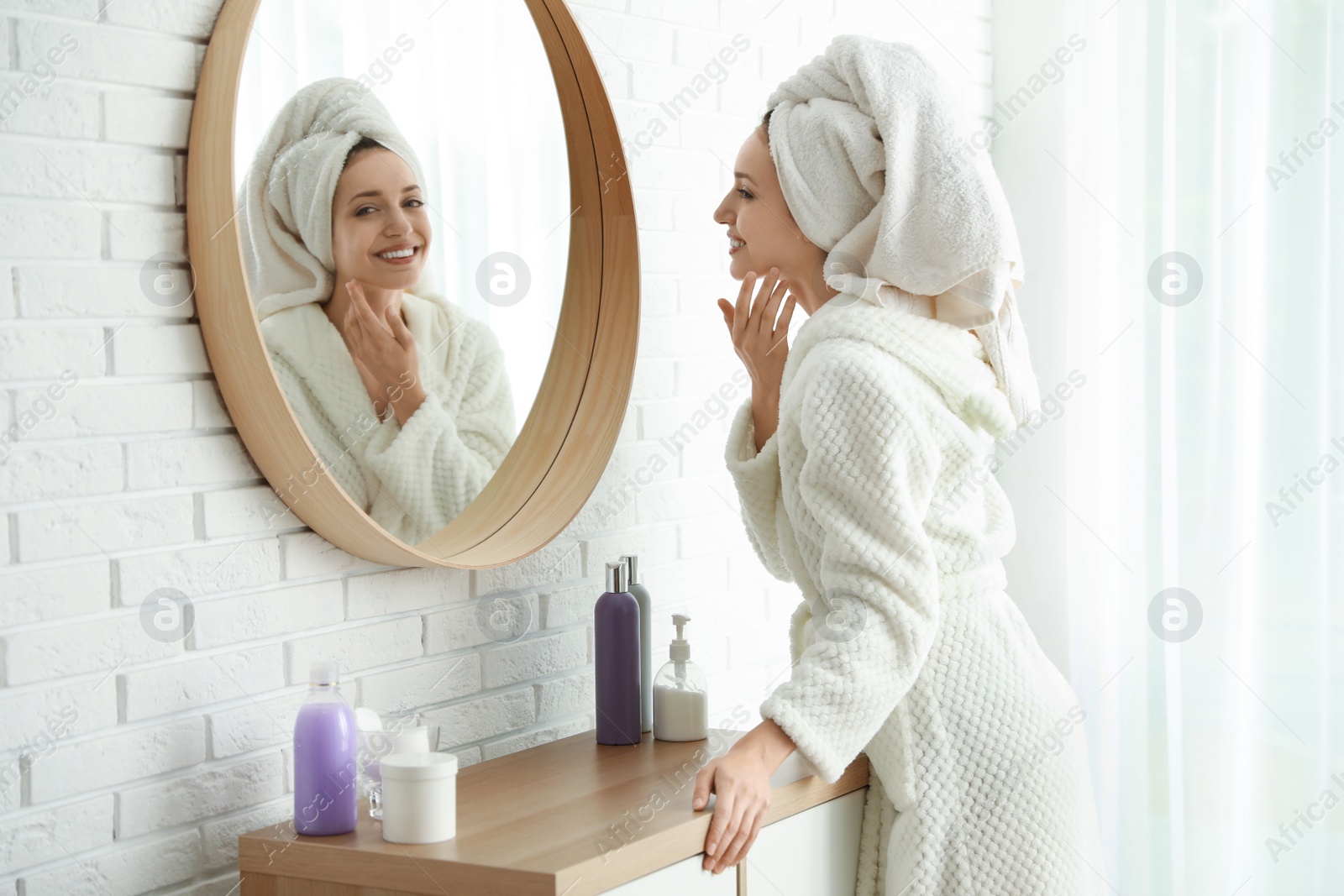 Photo of Pretty young woman with towel on head near mirror indoors