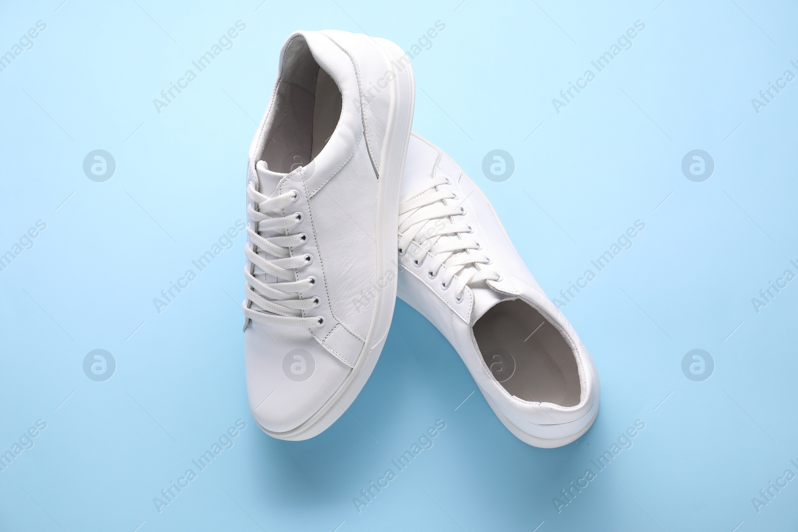 Photo of Pair of stylish white sneakers on light blue background, top view