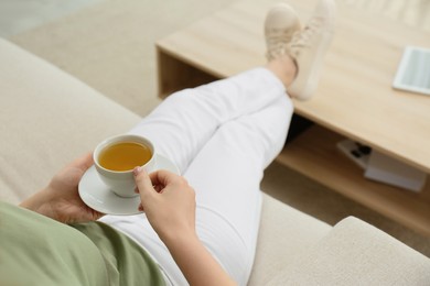 Young woman with cup of hot tea relaxing on sofa at home, closeup