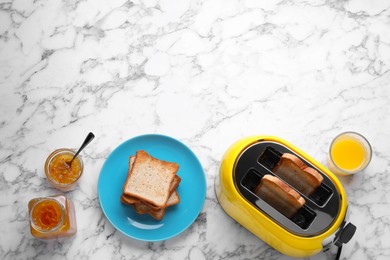 Photo of Yellow toaster with roasted bread, glass of juice and jam on white marble table, flat lay. Space for text