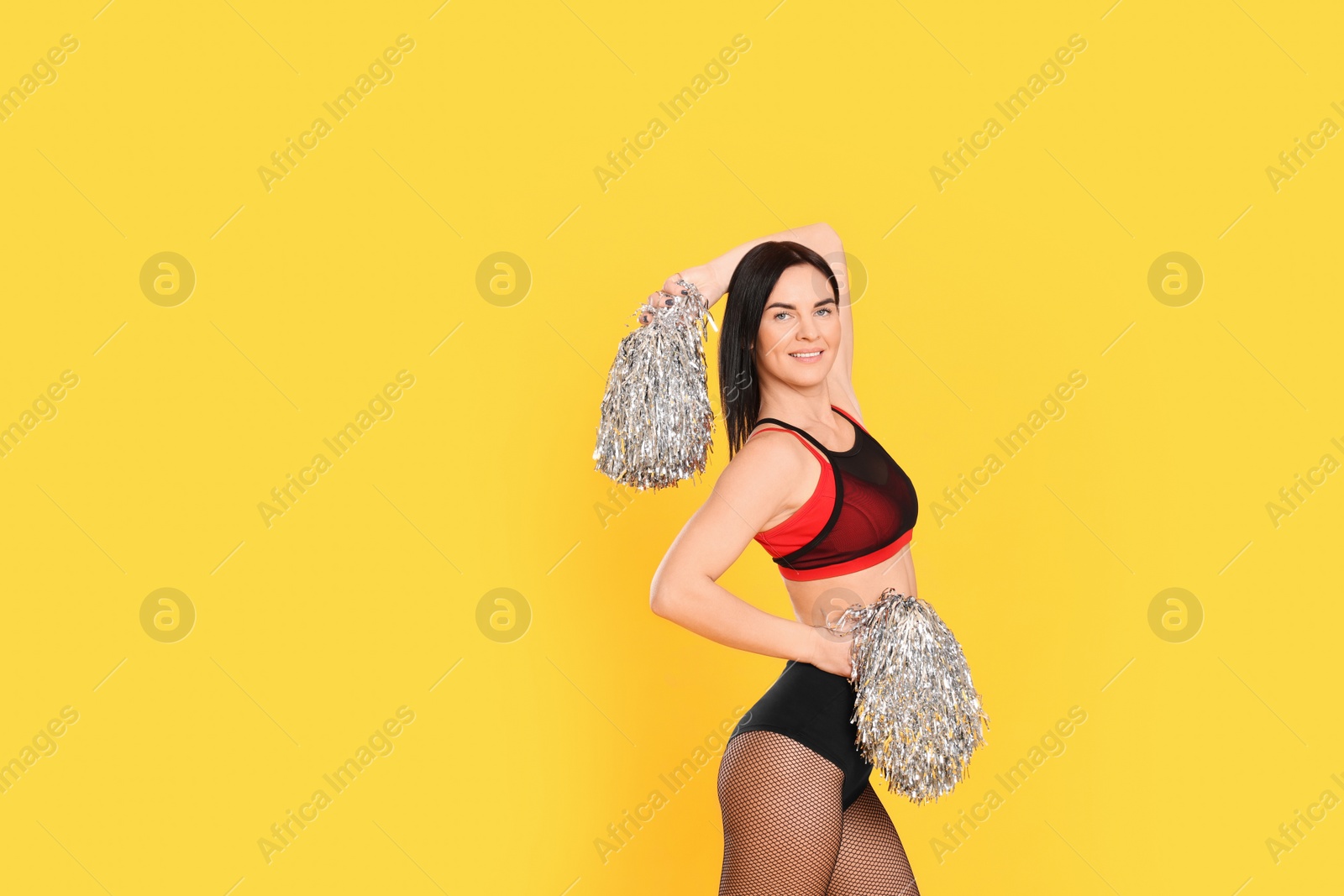 Photo of Beautiful cheerleader in costume holding pom poms on yellow background. Space for text