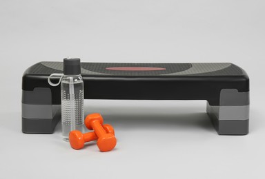 Photo of Step platform, dumbbells and water bottle on light background. Sport equipment