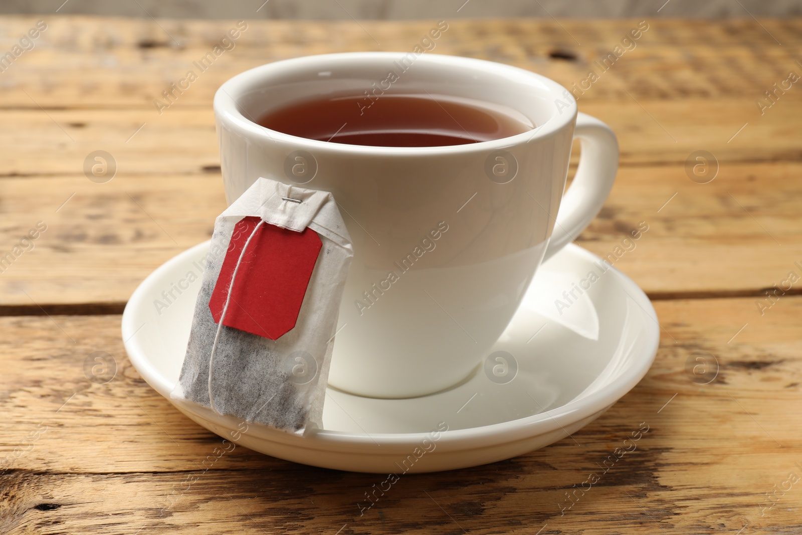 Photo of Tea bag and cup of hot beverage on wooden table, closeup