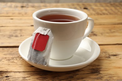 Photo of Tea bag and cup of hot beverage on wooden table, closeup