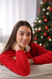 Portrait of smiling woman on sofa near Christmas tree at home