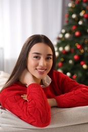 Photo of Portrait of smiling woman on sofa near Christmas tree at home