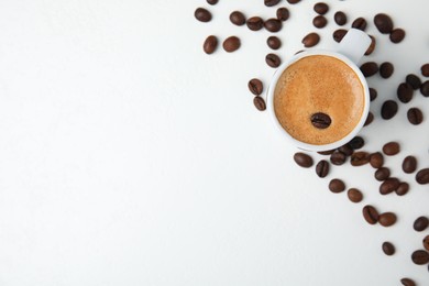 Photo of Cup of tasty espresso and scattered coffee beans on white table, flat lay. Space for text