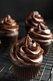 Photo of Cooling rack with delicious chocolate cupcakes on black table, closeup