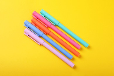 Many colorful markers on yellow background, flat lay