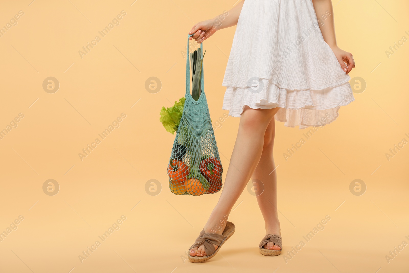 Photo of Woman with string bag of fresh vegetables on beige background, closeup. Space for text