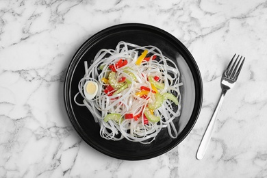 Photo of Plate of tasty rice noodles and fork on marble table, flat lay