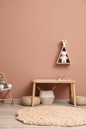 Photo of Cute child room interior with furniture, toys and wigwam shaped shelf on pink wall