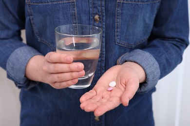 Photo of Woman with glass of water and pill on blurred background, closeup