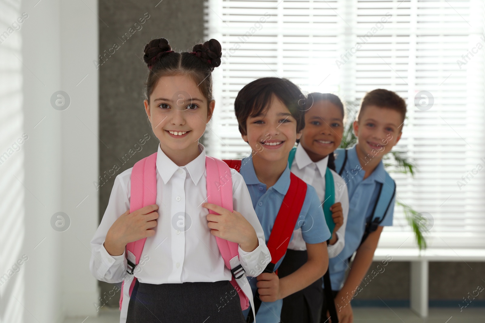 Photo of Happy children in school uniform with backpacks indoors