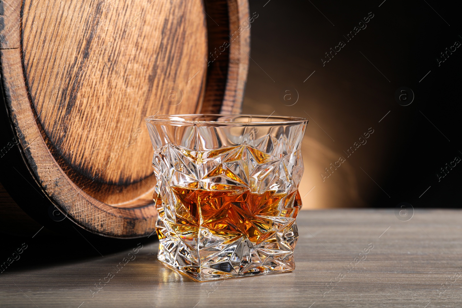 Photo of Glass with whiskey and wooden barrel on table, space for text