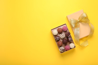 Photo of Open box with delicious chocolate candies on yellow background, top view. Space for text