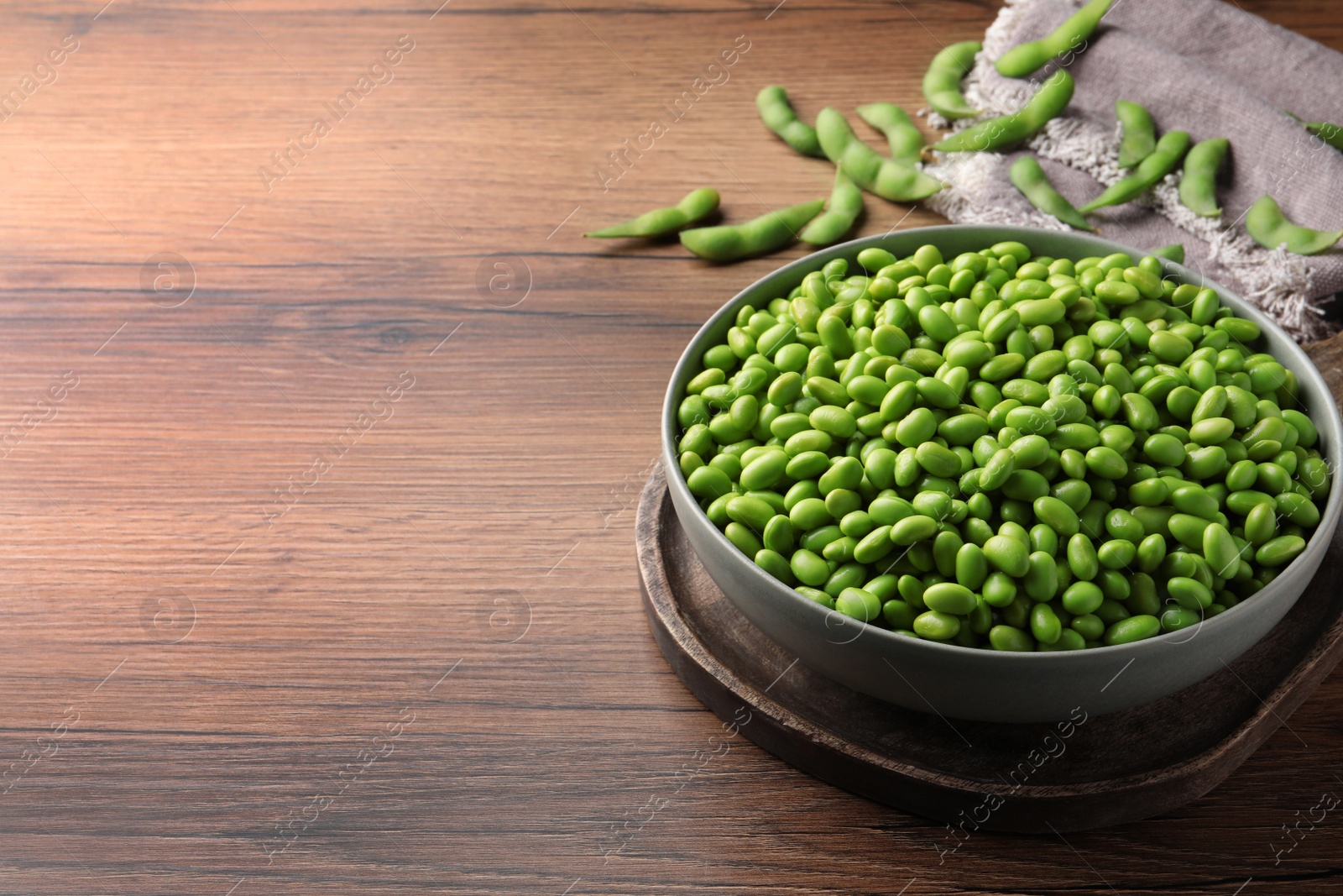 Photo of Bowl of delicious edamame beans on wooden table, space for text