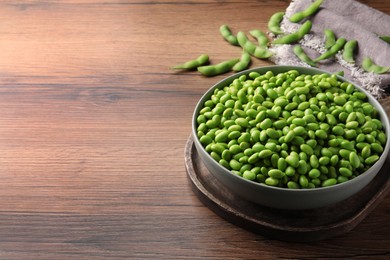 Bowl of delicious edamame beans on wooden table, space for text