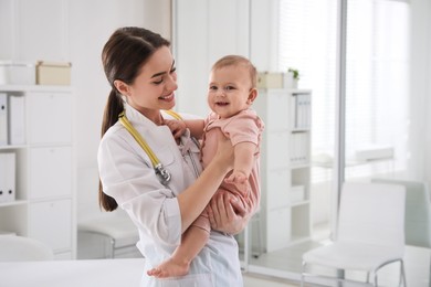 Photo of Young pediatrician with cute little baby in clinic. Space for text