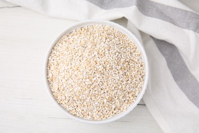 Photo of Dry barley groats in bowl on white wooden table, top view