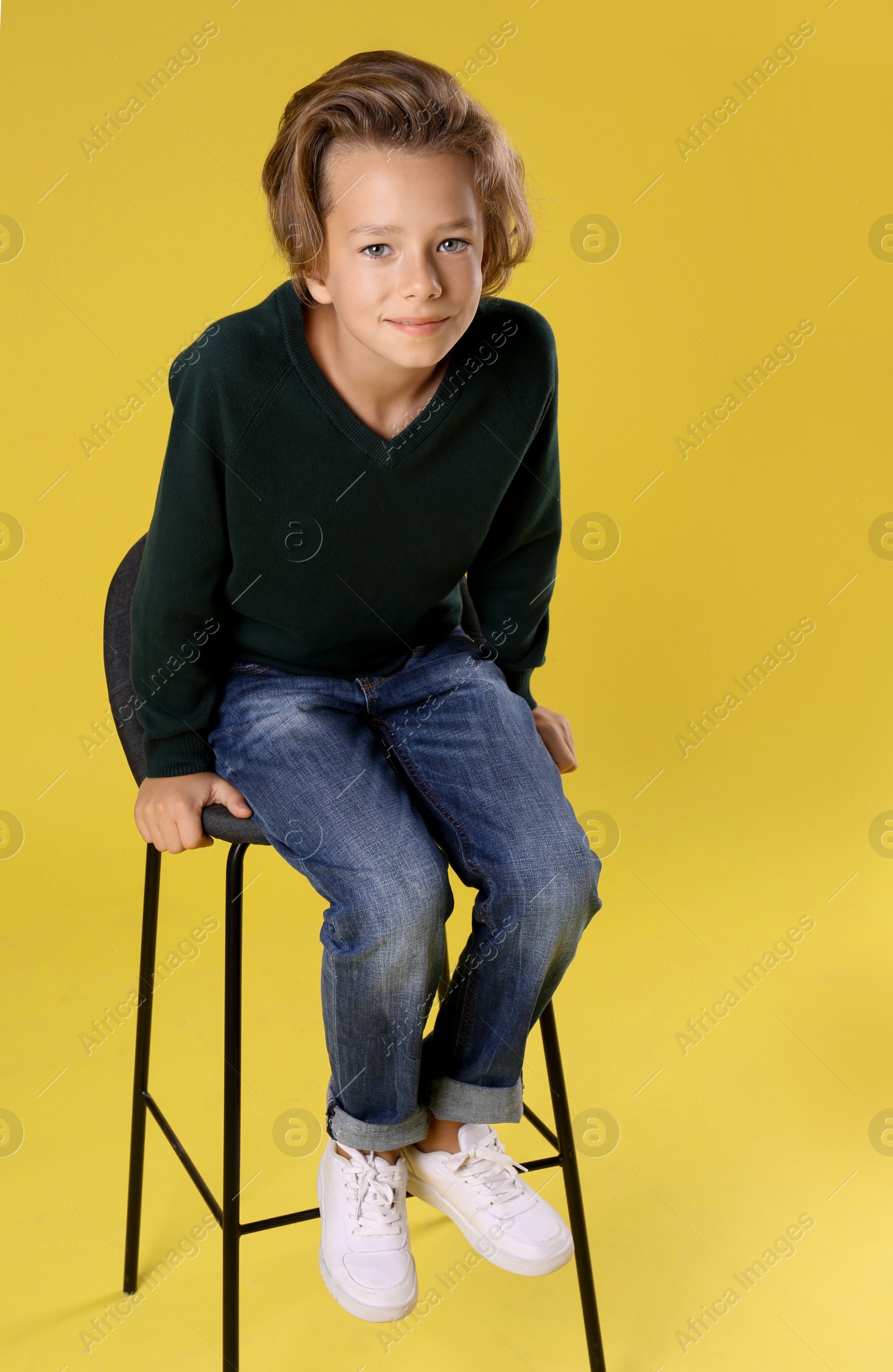 Photo of Cute little boy sitting in chair on yellow background