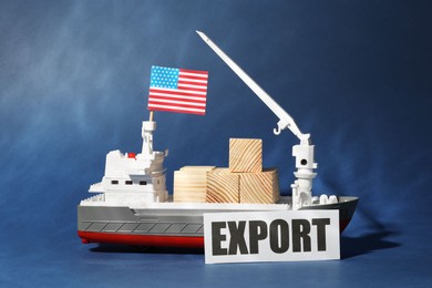 Photo of Toy cargo vessel with American flag and wooden cubes on blue background. Export concept