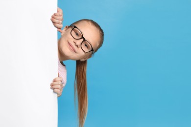 Photo of Cute girl looking out of placard against light blue background. Space for text