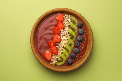 Bowl of delicious smoothie with fresh blueberries, strawberries, kiwi slices and oatmeal on light green background, top view