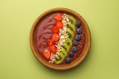 Photo of Bowl of delicious smoothie with fresh blueberries, strawberries, kiwi slices and oatmeal on light green background, top view