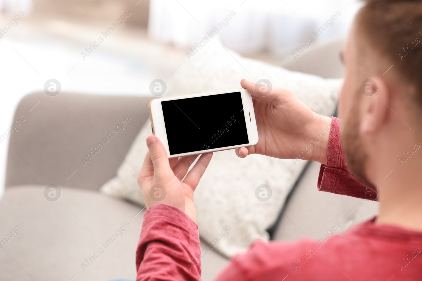 Photo of Young man using video chat on smartphone in living room, closeup. Space for design