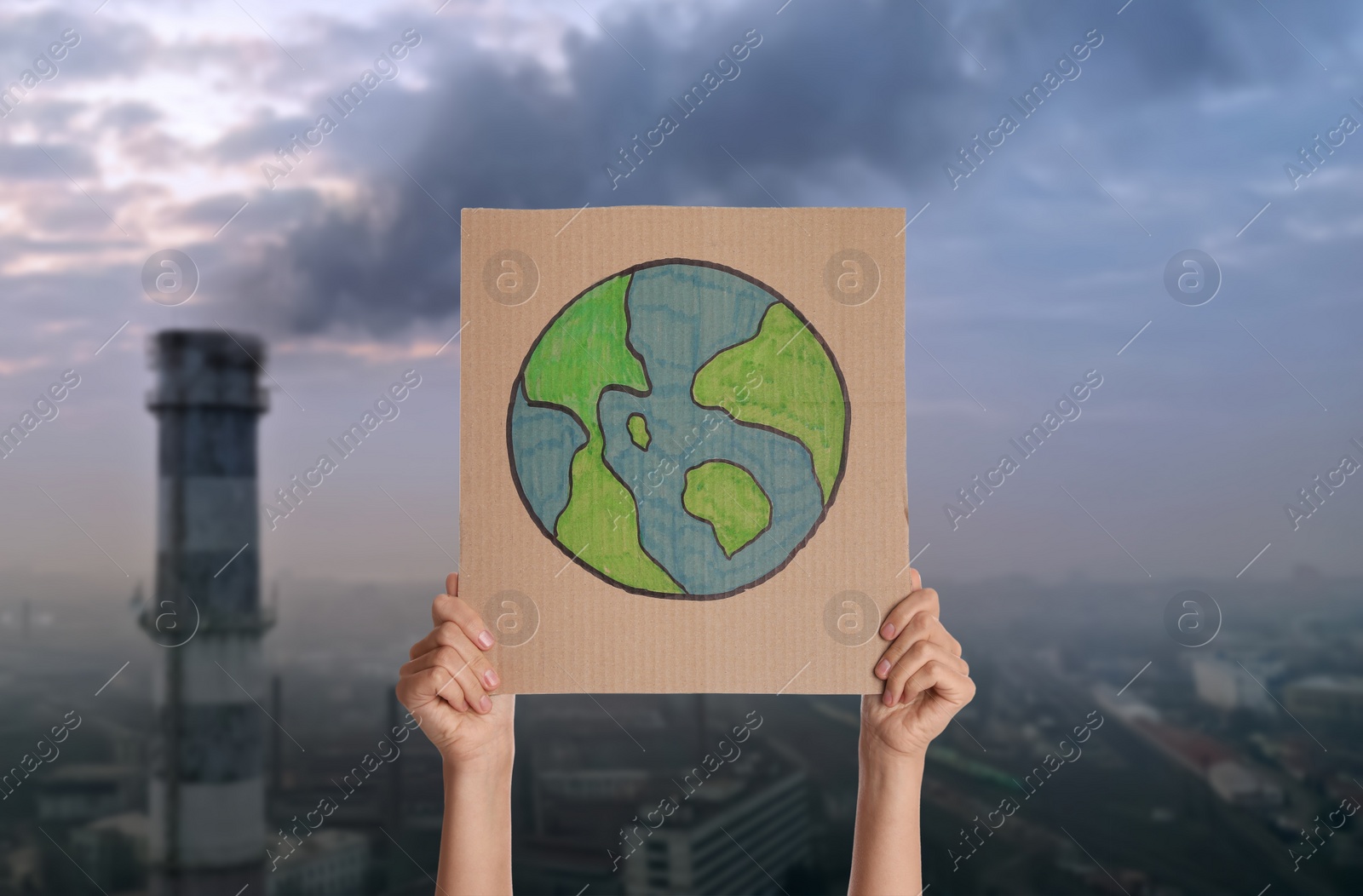 Image of Protestor holding placard with Earth drawing and blurred view of industrial factory on background. Climate strike