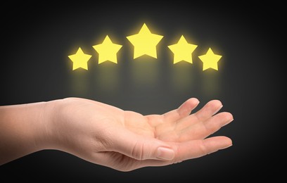 Image of Woman holding virtual stars on black background, closeup. Customer satisfaction score