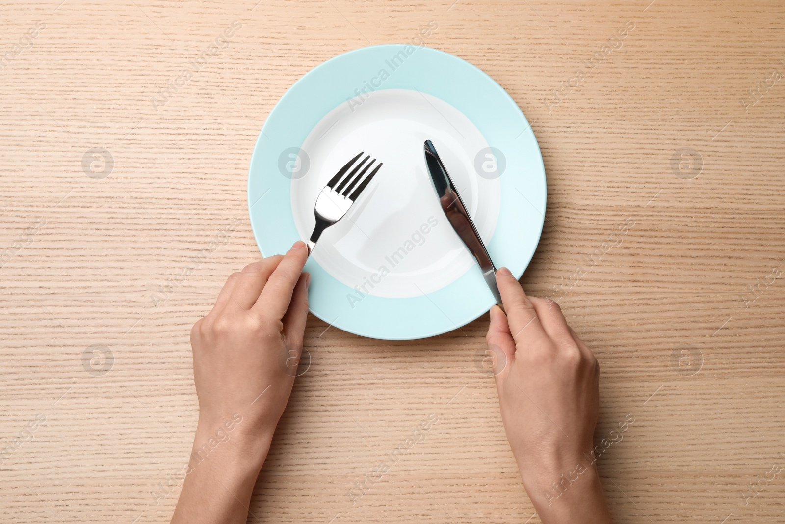 Photo of Woman with empty plate and cutlery at wooden table, top view