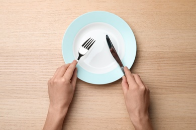 Photo of Woman with empty plate and cutlery at wooden table, top view