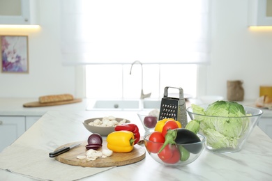 Different fresh vegetables and mushrooms on white table in modern kitchen. Space for text