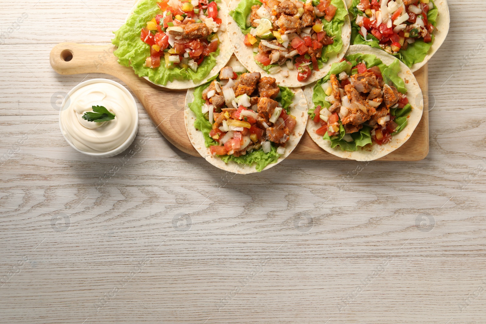 Photo of Delicious tacos with vegetables, meat and sauce on white wooden table, top view. Space for text