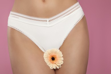 Photo of Woman in white panties with gerbera flower on pink background, closeup