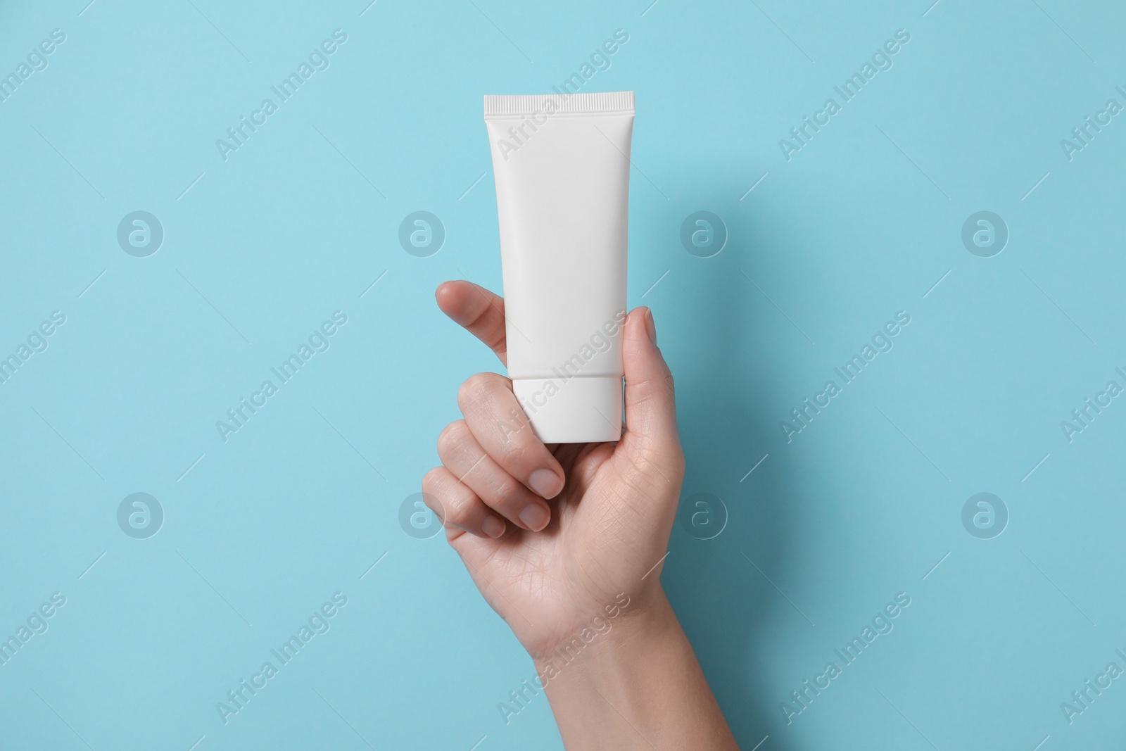 Photo of Woman with tube of hand cream on light blue background, top view