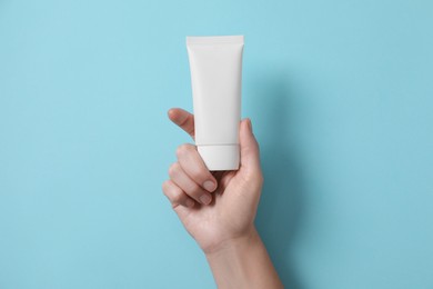 Woman with tube of hand cream on light blue background, top view