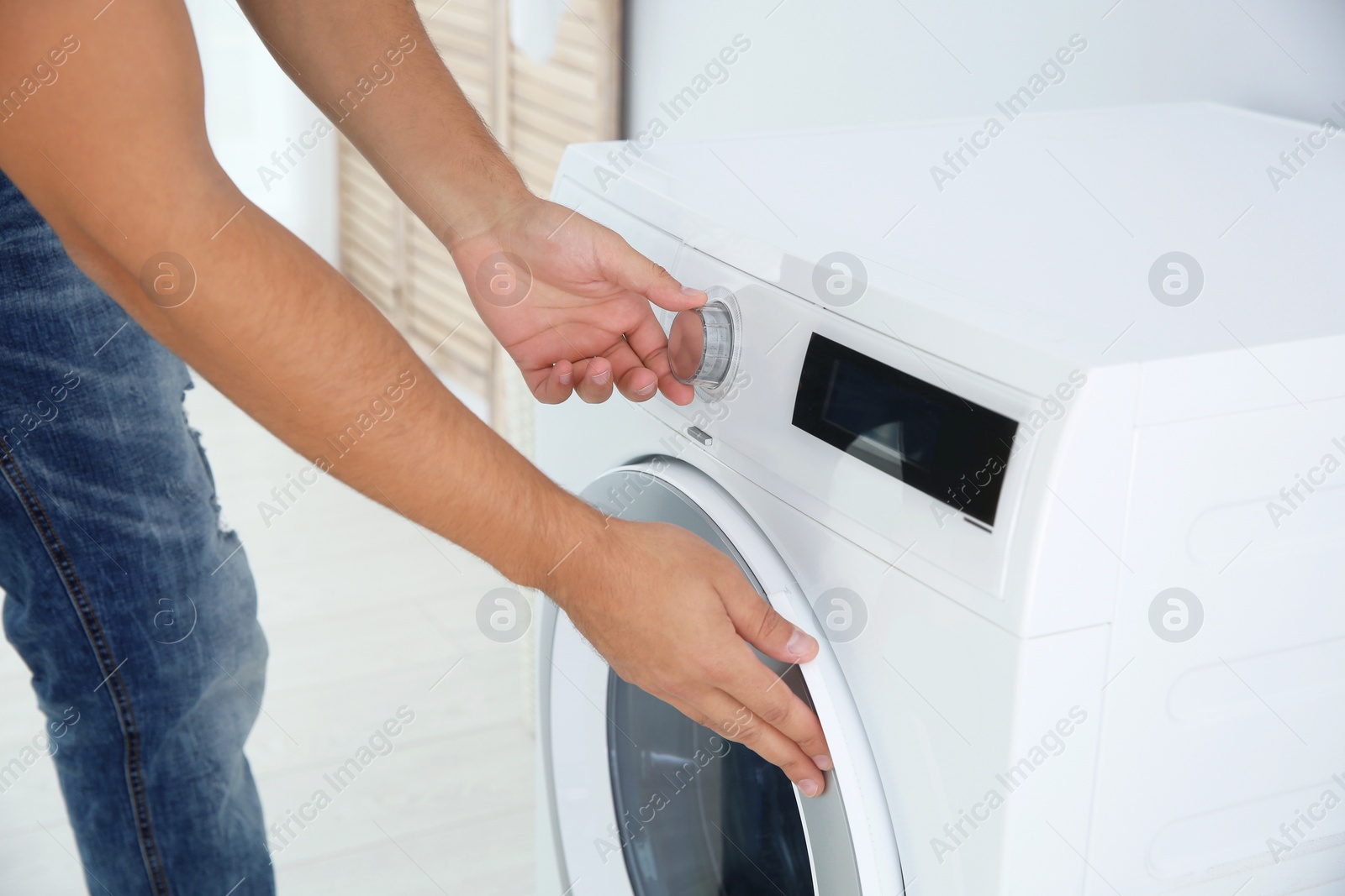 Photo of Young man using washing machine, closeup. Laundry day