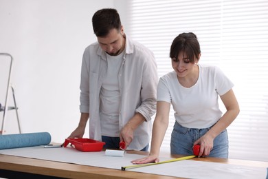 Woman and man applying glue onto wallpaper sheet at wooden table indoors